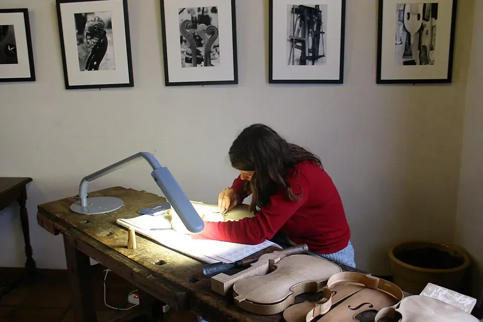 Un jeune élève luthier en démonstration devant le public, penché sur une pièce de violon en cours de fabrication