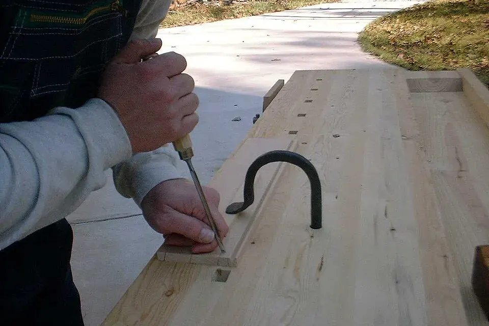 Un valet d'établi en métal maintient une pièce de bois sur le plateau d'un établi de menuisier