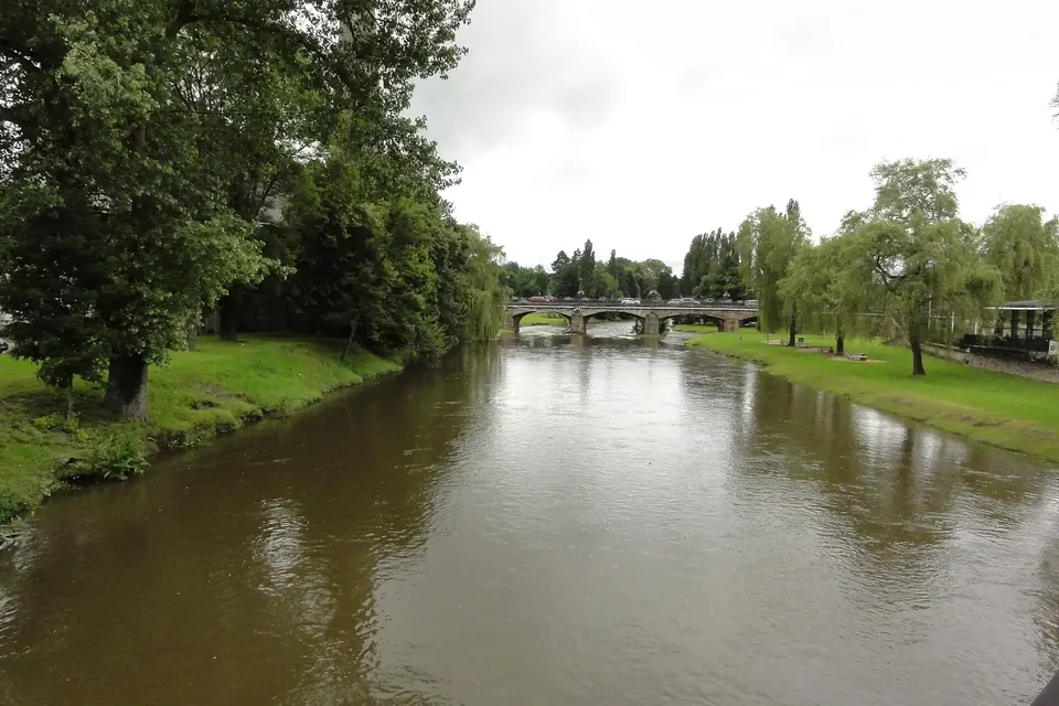 La Meurthe à Baccarat : une rivière calme bordée d'arbres et de pelouses, un pont de pierre au loin