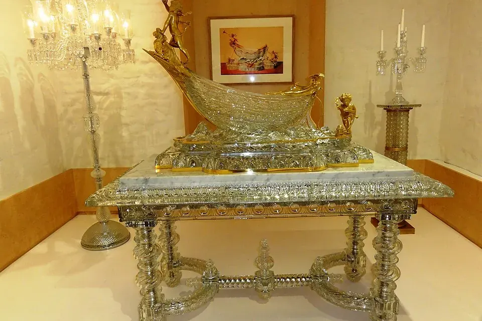 Salle du musée de la cristallerie de Baccarat : une table et une grande pièce de cristal taillé posées devant un mur clair, encadrées de candélabres en cristal
