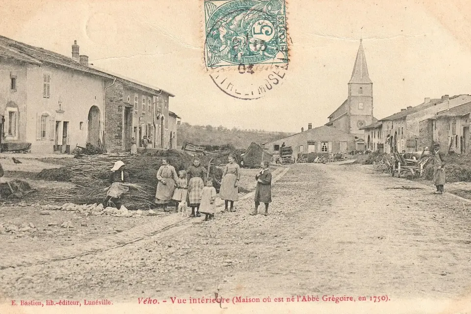 Carte postale ancienne d'une rue de village lorrain bordée de maisons avec grandes portes de grange